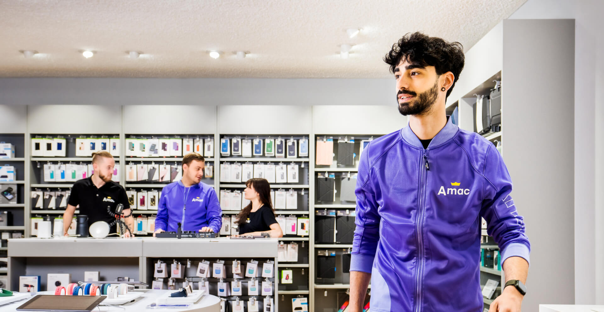 Amac 1920×992 Medewerkers van Amac aan het werk in de winkel gekleed in een zwarte Amac-polo, T-shirt en full custom made Amac-jasje in de kenmerkende paarse Amac-kleur