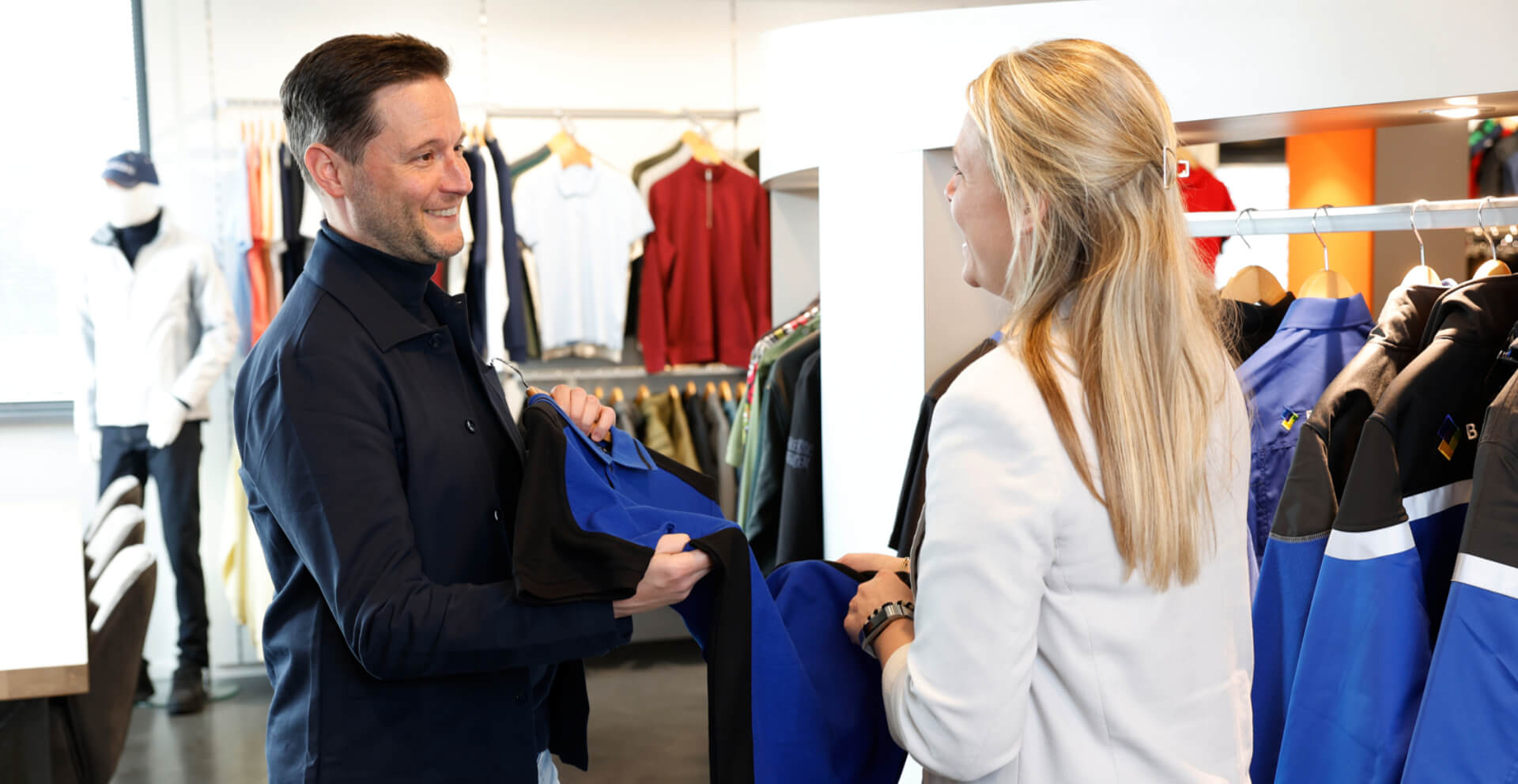 Showroom 1920×992 Klant bekijkt de mogelijkheden voor het personaliseren of ontwerpen van bedrijfskleding in de showroom van Outfit company wear