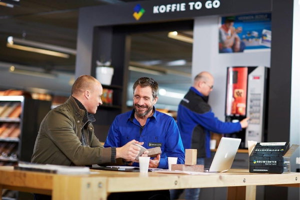 Bouwcenter 600×400 Medewerker van Bouwcenter in Bouwcenter-bedrijfskleding door Outfit company wear helpt een klant in de winkel