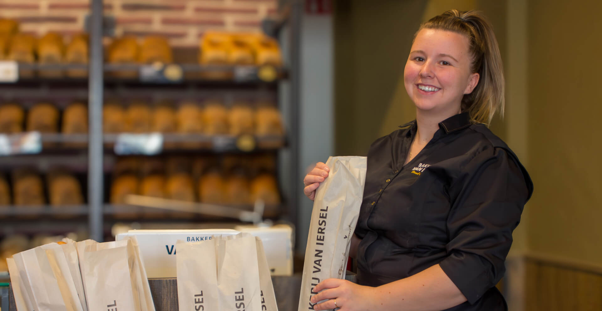 Bakkerij van Iersel 1920×992 Medewerker van Bakkerij van Iersel aan het werk in de winkel in bedrijfskleding gemaakt door Outfit company wear