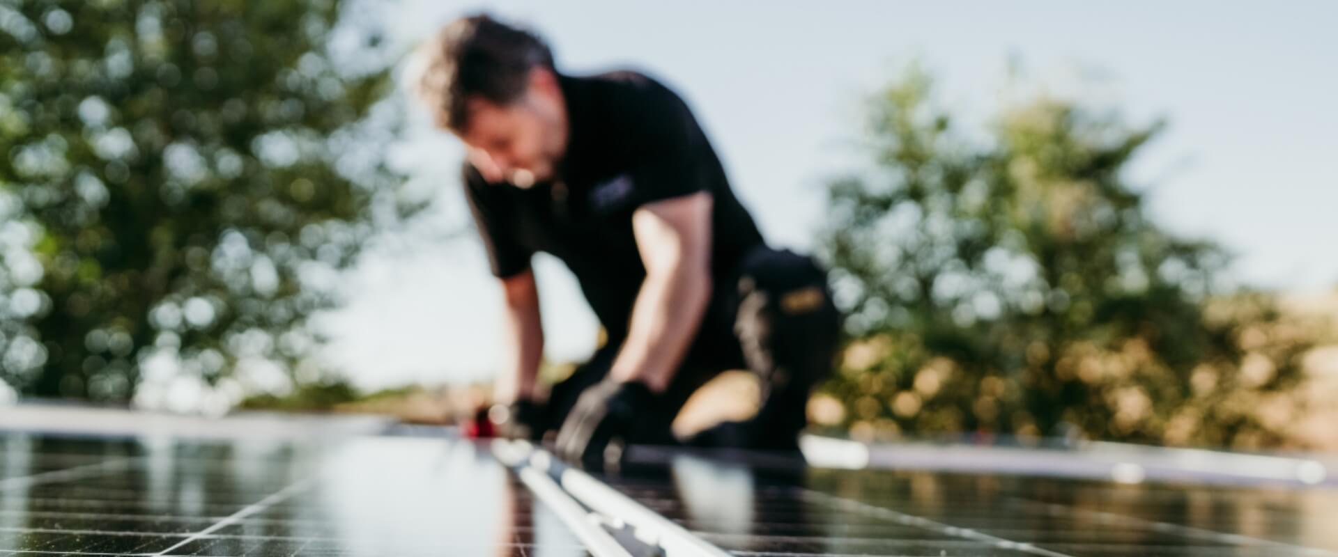 Werken in de zon headerfoto Man in werkkleding installeert zonnepanelen op een warme dag - Blog: bescherm jezelf tegen de zon met deze tips van Outfit company wear