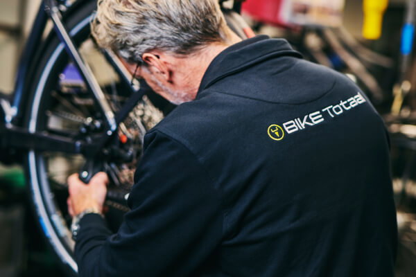 Bike Totaal medewerker Medewerker van Bike Totaal repareert een fiets in de winkel gekleed in smart custom made-bedrijfskleding door Outfit company wear